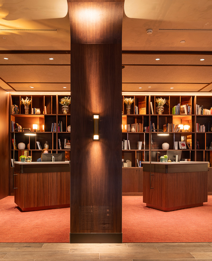 Mostradores de recepción gemelos en madera oscura con una gran columna central iluminada detrás.