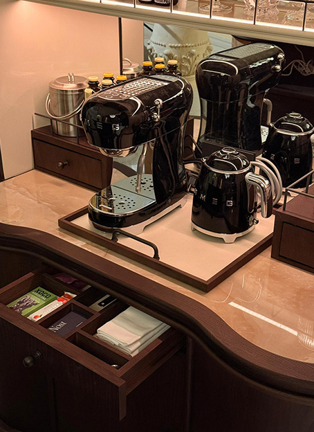 Cafetera y tetera Smeg negras sobre encimera con cajón de organización de café abierto.