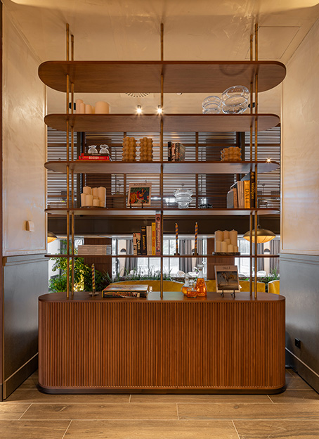 Estantería divisoria de madera con libros, velas y objetos decorativos en un salón elegante.