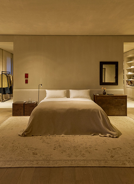 Dormitorio de estilo rústico elegante con cama de matrimonio, mesitas de madera, espejo y estanterías integradas en la pared.