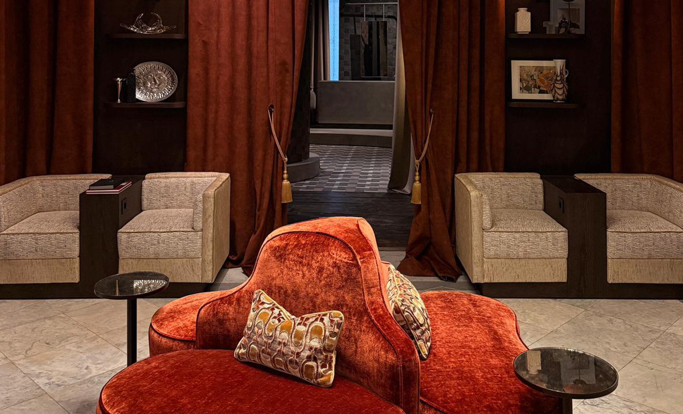 Sofá central rojo rodeado simétricamente por cuatro sillones beige y grandes cortinas rojizas.