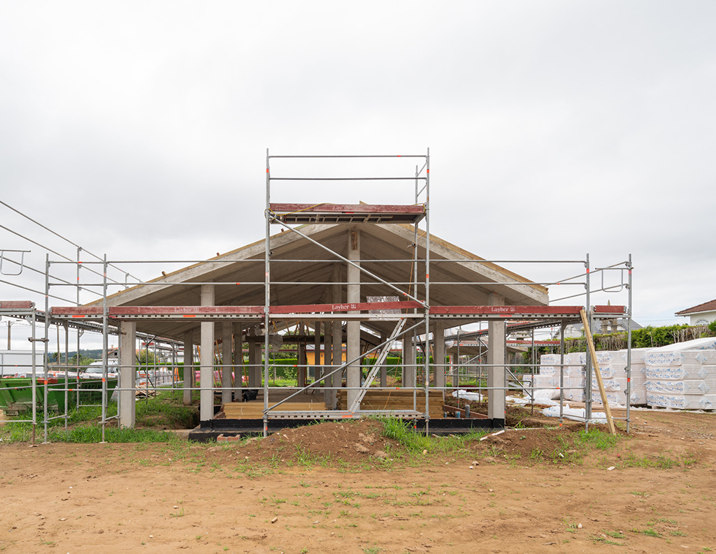El exterior de una estructura de hormigón en construcción, rodeada de andamios y materiales.