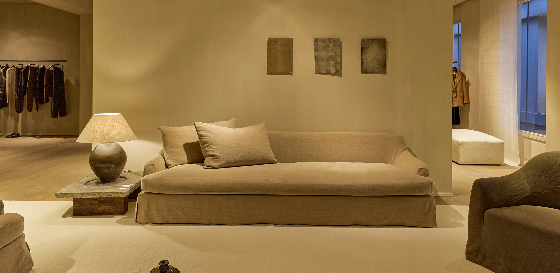 Zona de descanso con sofá de lino, lámpara de mesa rústica y cuadros abstractos en una pared color crema.