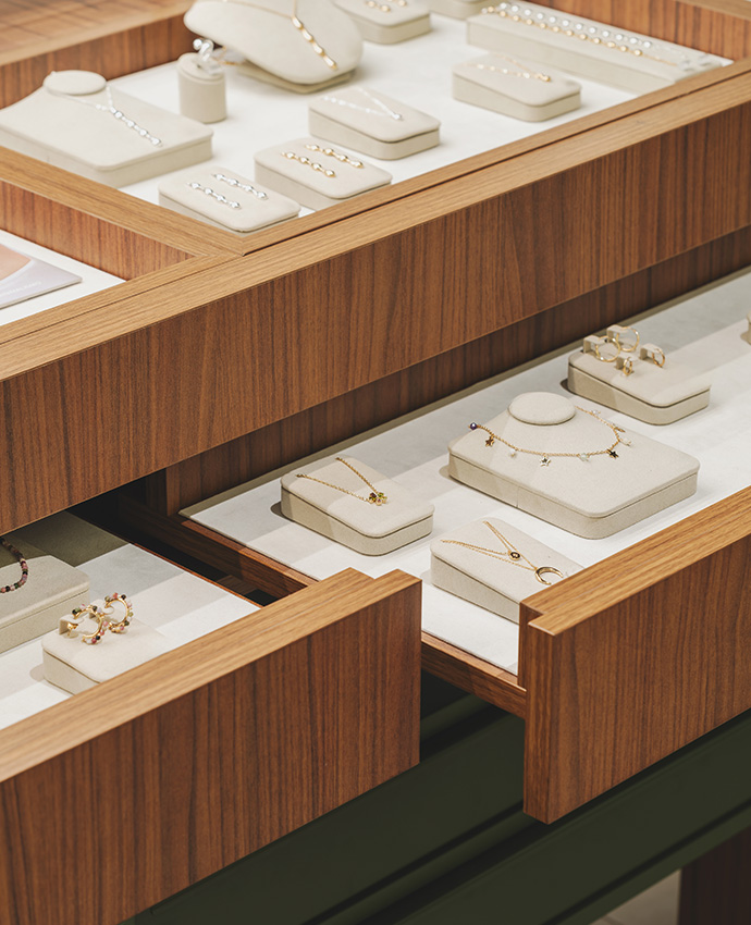 Primer plano de cajones de madera abiertos con delicados soportes para collares y valiosos anillos.