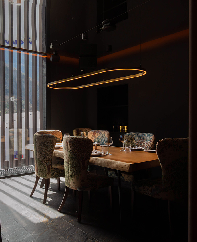 Elegante comedor privado con sillas de respaldos estampados junto a una ventana iluminada por lámpara de diseño.