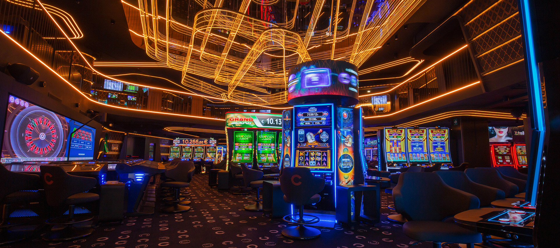 Interior de un casino moderno con máquinas tragaperras y líneas de luces naranjas en el techo oscuro.