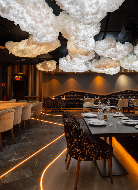 Restaurante decorado con lámparas que imitan nubes esponjosas y un camino luminoso naranja en el suelo gris.