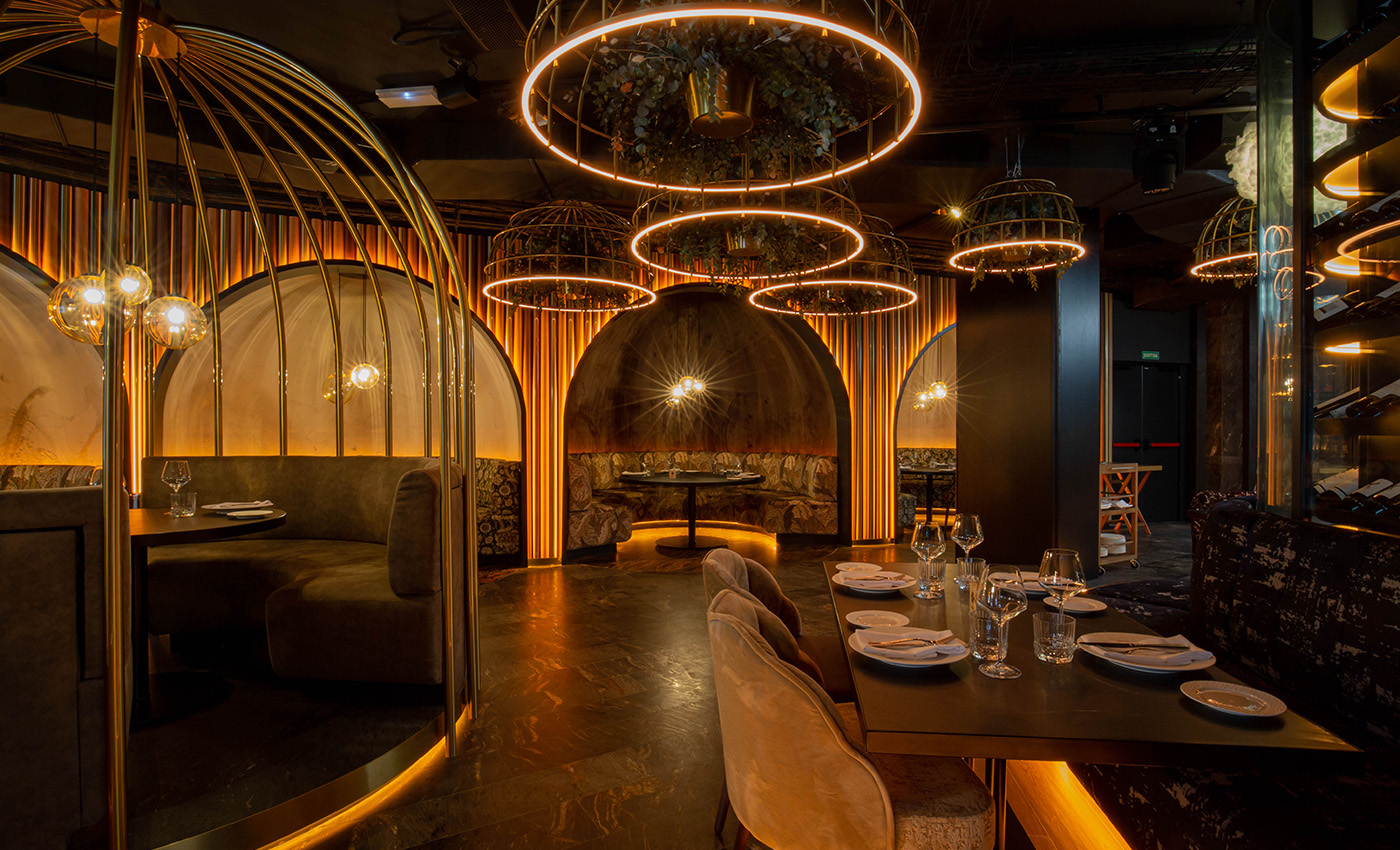 Restaurante de lujo con reservados circulares en forma de jaulas doradas y mesas preparadas para los comensales.