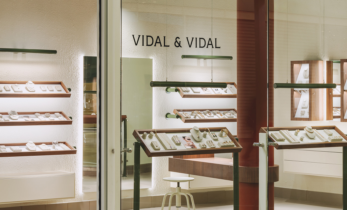 Escaparate acristalado de la tienda que revela elegantes exhibidores de joyas y un taburete blanco.
