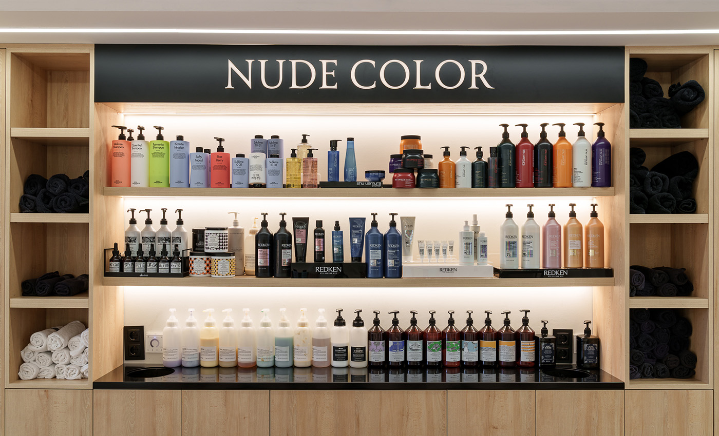 Estantería de madera iluminada con productos de peluquería, botes de champú organizados por colores y toallas enrolladas a los lados.