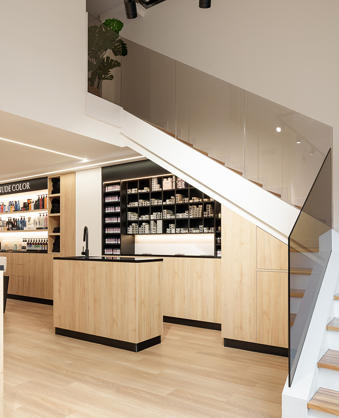 Zona interior con un mostrador de madera, un lavabo negro con grifo alto y una escalera moderna con barandilla de cristal transparente.