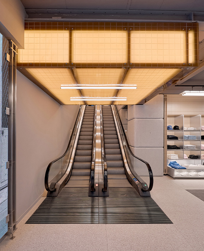 Escaleras mecánicas de una tienda moderna situadas bajo un techo luminoso de rejilla amarilla y acabado industrial.