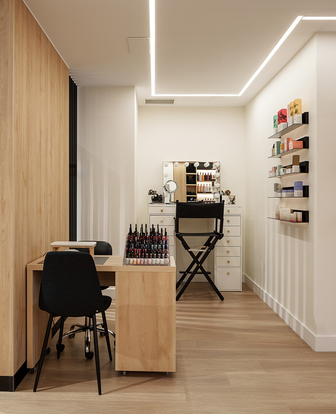 Espacio dedicado a manicura y maquillaje, con una mesa de madera clara, sillas negras y un tocador con luces integradas.