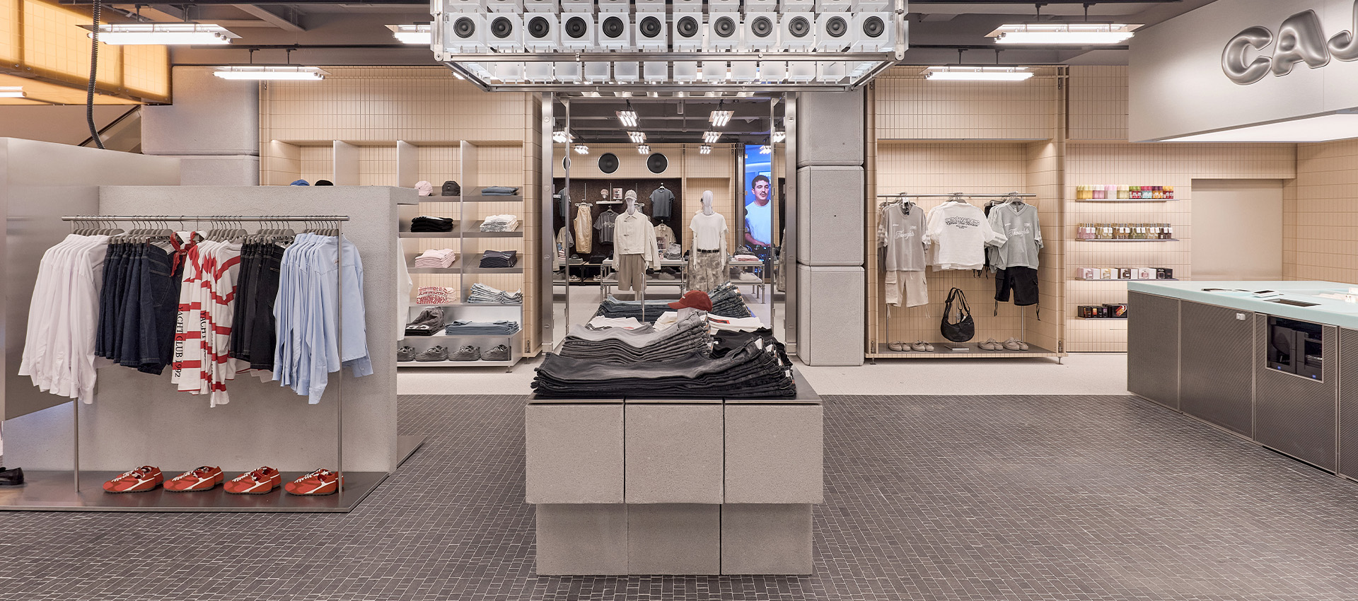 Espacio comercial amplio con ropa expuesta en mesas centrales, percheros laterales, piso cerámico y zona de cajas.