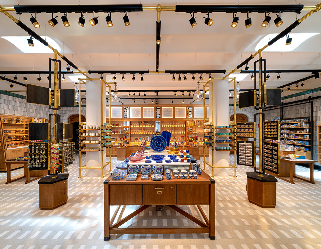 Tienda de recuerdos amplia con acabados dorados, suelo decorado, columnas blancas y estanterías llenas de coloridos objetos artesanales.