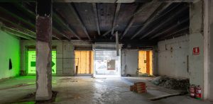 Espacio comercial interior completamente diáfano en plena fase de reforma con pilares de hormigón y materiales acumulados.