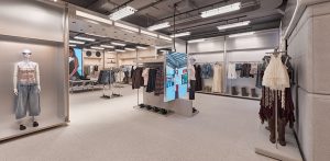 Boutique de ropa moderna y espaciosa, con estructuras metálicas, iluminación industrial, maniquíes y pantallas digitales en el centro.