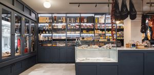Comercio de alimentación gourmet con estanterías de color azul oscuro, iluminación LED, embutidos colgados y vitrinas.