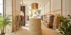 Tienda de ropa estilo boho-chic con estructuras de madera clara, plantas naturales, cálida iluminación y suelo de piedra.
