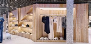 Expositor de moda con paneles de madera clara, luz indirecta integrada, ropa colgada ordenada y calzado muy bien exhibido.