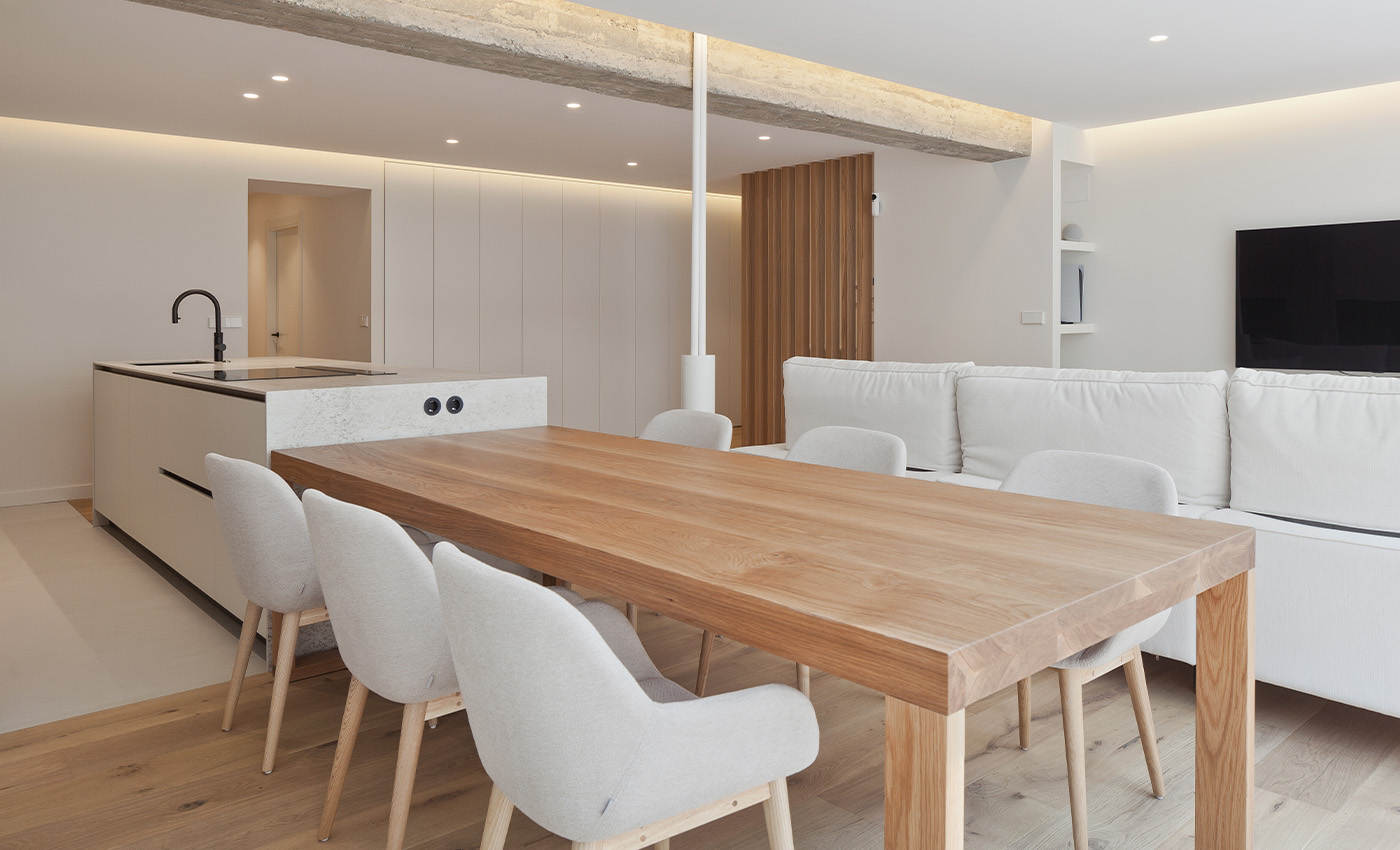 Amplio espacio abierto que integra la cocina con isla, un gran comedor con mesa de madera y el salón con sofá blanco.