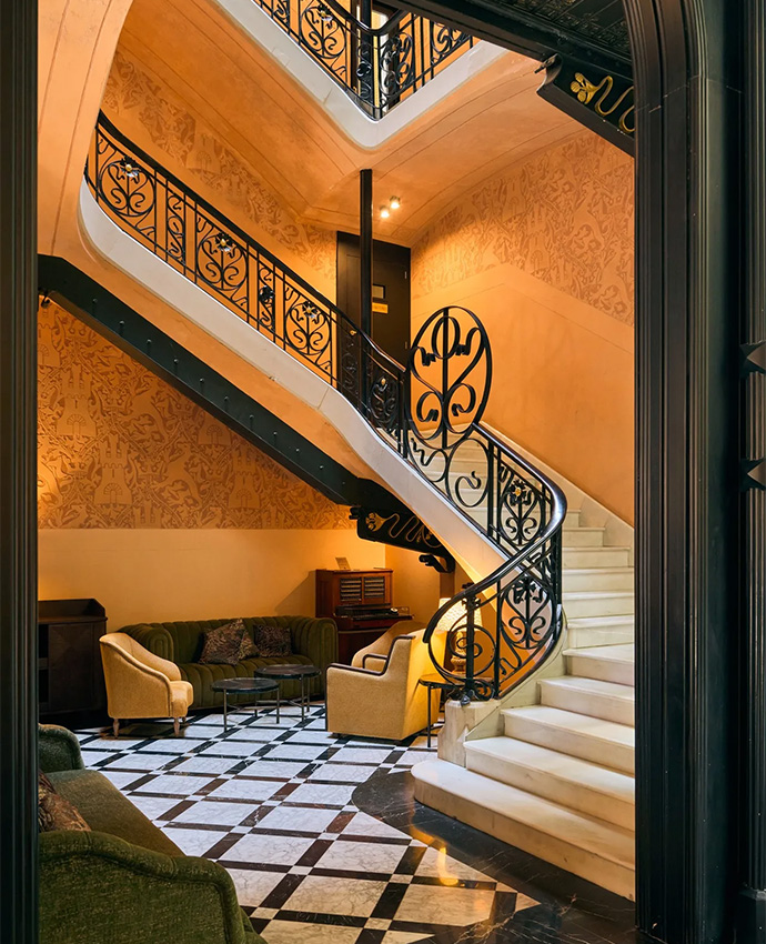 Elegante escalera interior con barandilla de hierro forjado, suelo ajedrezado y paredes doradas