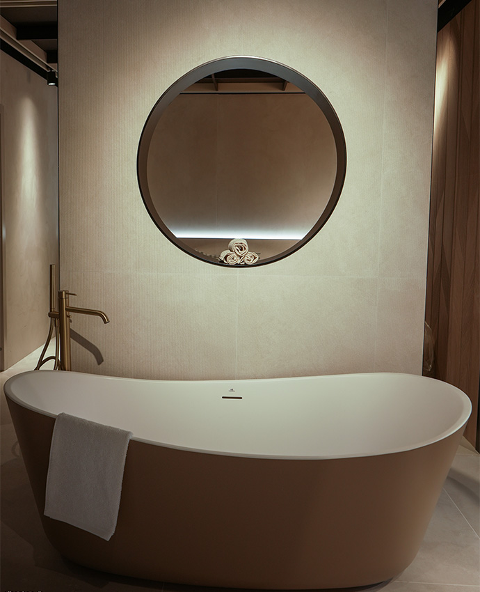 Elegante bañera exógena beige bajo un espejo circular iluminado, combinada con grifería dorada moderna.