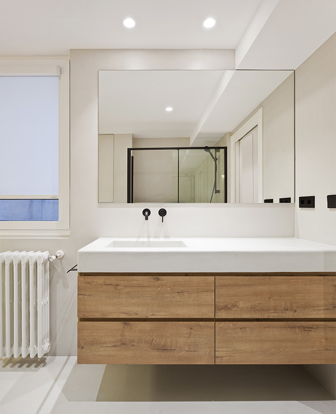 Cuarto de baño moderno con mueble flotante de madera, gran espejo de pared, grifería negra empotrada y radiador clásico blanco.
