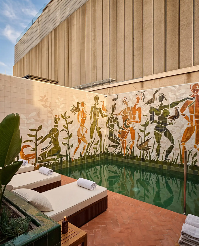 Piscina exterior rodeada por un mural de azulejos artísticos y cómodas tumbonas beige.