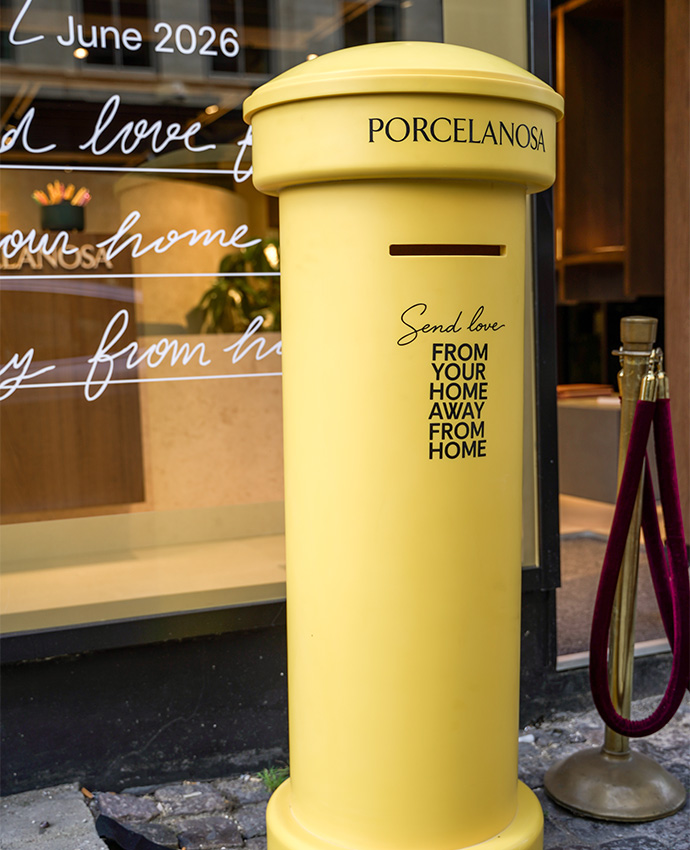 Un buzón postal amarillo brillante con texto publicitario decorativo ubicado afuera de una tienda elegante.