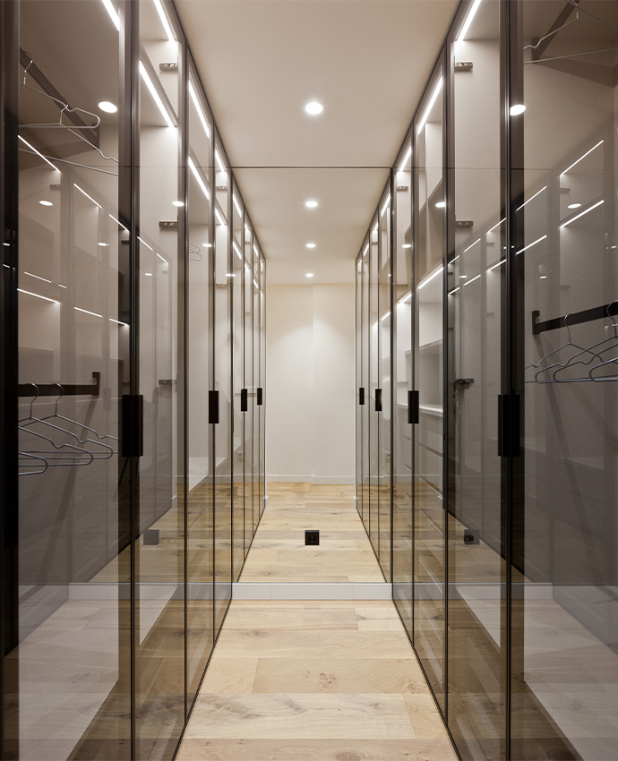 Pasillo vestidor simétrico con armarios de puertas de cristal oscuro y perchas iluminadas con luz LED integrada.