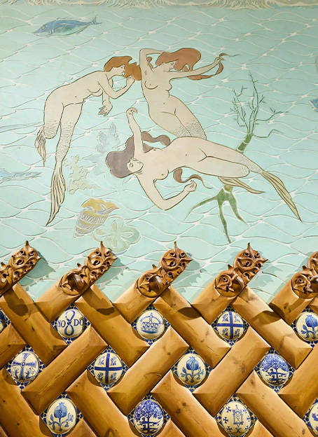 Detalle de un mural pintado con sirenas nadando sobre un fondo marino de azulejos.