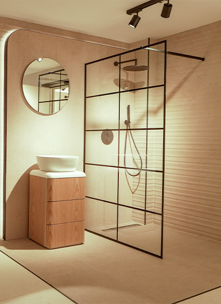 Baño contemporáneo con mampara de vidrio en cuadrícula negra, lavabo sobre mueble y espejo circular.