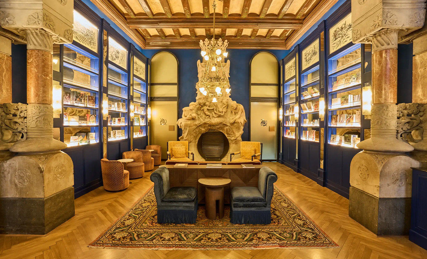 Sala de estar señorial con chimenea esculpida, estanterías azules iluminadas y alfombra clásica.