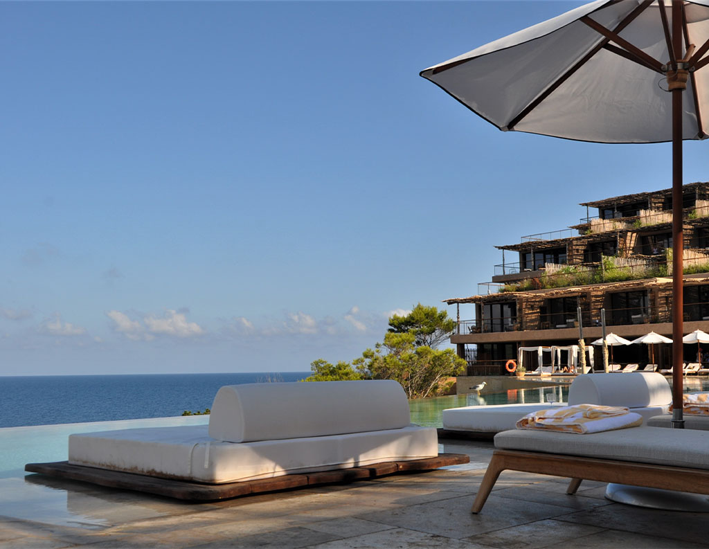 Terraza de resort de lujo frente al mar, con tumbonas, sombrilla, piscina con vistas al océano y arquitectura moderna