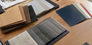 Muestrario de materiales sobre madera, con láminas de madera, telas textiles grises y paleta de colores.