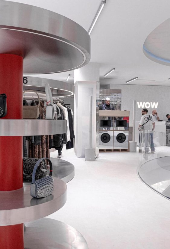 Interior de tienda de moda con expositores circulares metálicos y señal "WOW" al fondo.