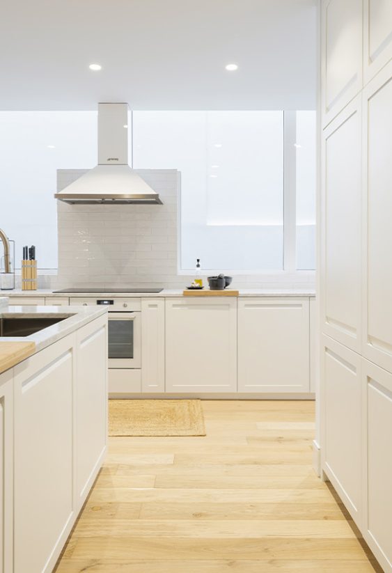 Cocina blanca con isla central, fregadero empotrado y suelo de madera clara