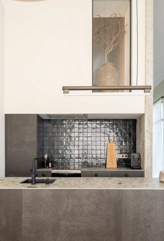 Cocina contemporánea con encimera de piedra, salpicadero negro y luz natural.