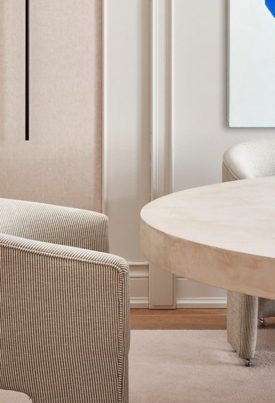 Sala de reuniones con mesa redonda clara, sillas tapizadas en crema y obra de arte azul en la pared