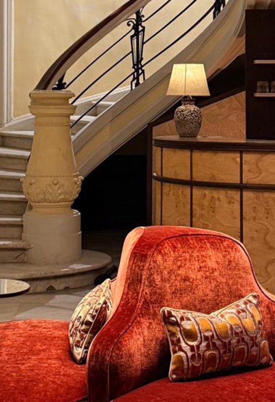 Sofá de terciopelo rojo en primer plano con una majestuosa escalera de mármol detrás.
