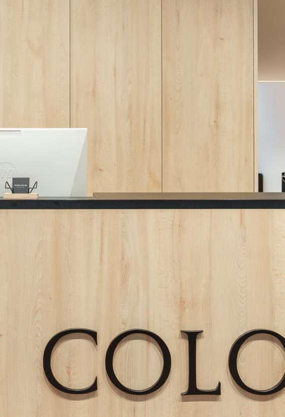 Mostrador de recepción de madera con el logotipo Nude Color en grandes letras oscuras y un ordenador blanco encima.