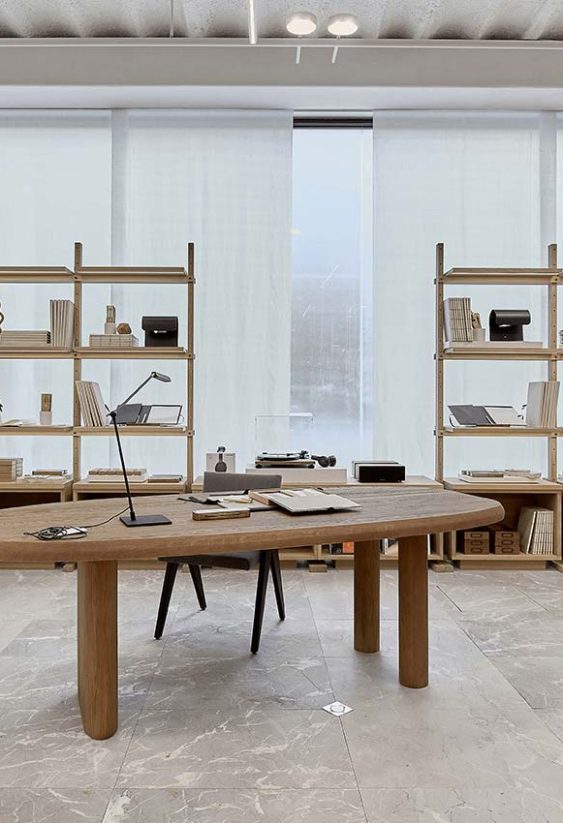 Showroom de diseño con estanterías de madera que exhiben objetos y mesa central sobre suelo de mármol claro.