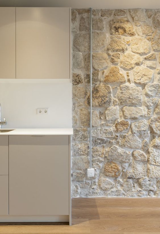 Cocina minimalista con muebles bajos beige y pared de piedra sobre suelo de madera.