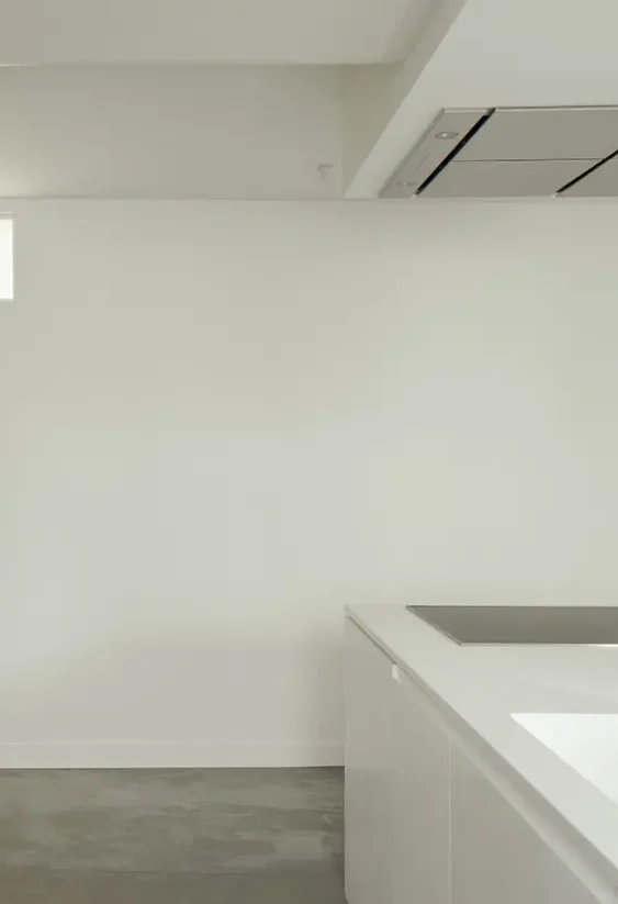 Cocina minimalista blanca con encimera integrada, mueble alto de madera y campana empotrada.