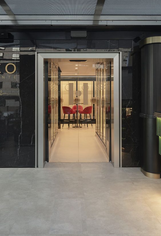 Fachada del restaurante Hünico con muro negro brillante, logotipo dorado y entrada central adyacente a barra iluminada.