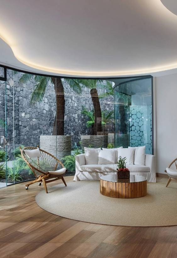 Salón contemporáneo con sofá crema, mesa de centro de cristal y ventanal panorámico al jardín.