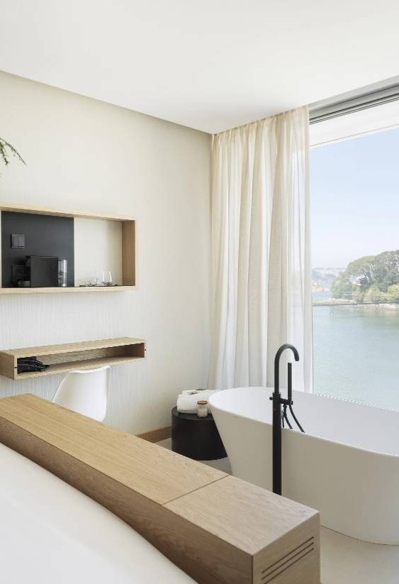 Dormitorio minimalista con bañera junto a ventanales panorámicos con vista al mar.
